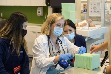 professor showing two students how to perform a clinical procedure during a simulation exercise