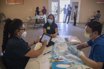 Maria Jaime, a health educator with the UArizona College of Public Health in Phoenix, goes through a patient’s answers on her registration for a COVID-19 vaccine, while Alvin Wong, DO, clinical associate professor of internal medicine with the UArizona College of Medicine – Phoenix, prepares her shot.