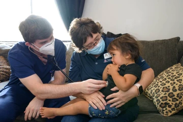 Dr. Hunt holds Amara Lopez while Winkleman listens to her heart during a home health visit.