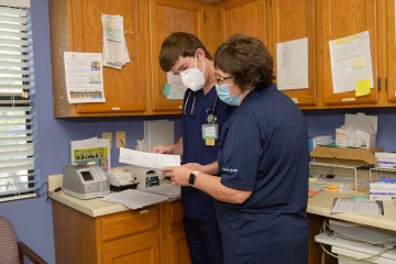 man and woman dressed in doctor scrubs stand in a medical clinic