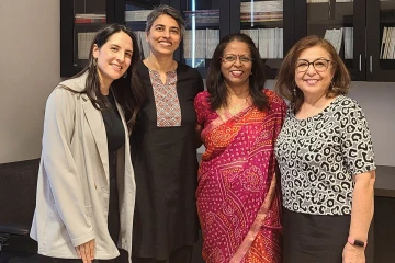 Three women standing together smiling. Two of the women are wearing traditional Indian clothing.