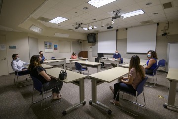 Six students and a professor sit in a classroom, separated by at least six feet and wearing masks. 