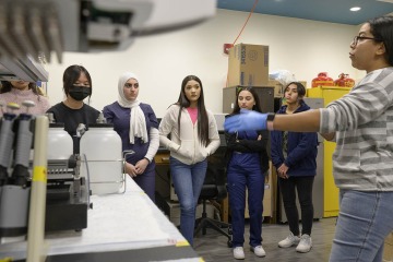 Female researcher shows students a robotic liquid handling system in a laboratory.