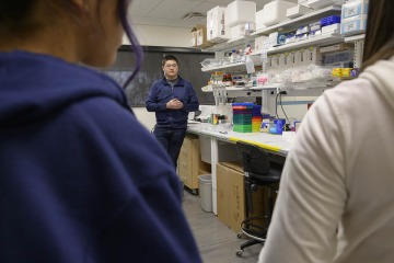Male researcher talks to students in a lab.