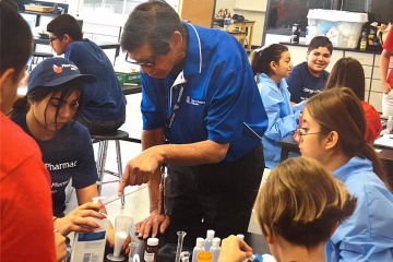 An Asian man wearing a blue polo t-shirt teaches middle school students about different types of chemicals.