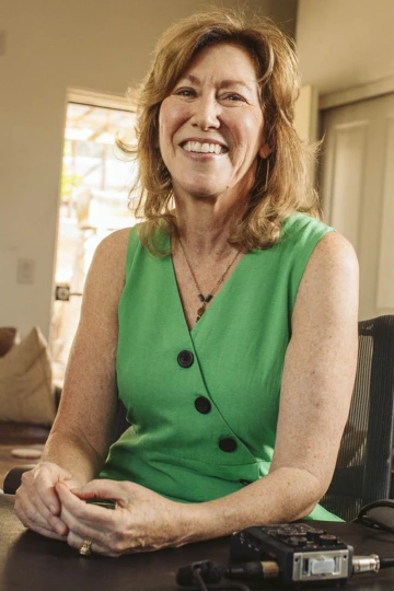 Older woman with shoulder-length brown hair wearing a green top and smiling