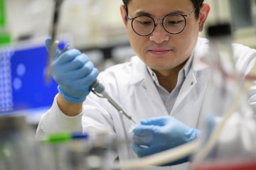 Asian man using a pipette in a lab setting.