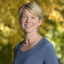 Portrait of Felicia Goodrum, a white woman with short blonde hair, standing outside wearing a dark blue blouse and smiling. 