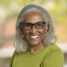 Portrait of Juanita Merchant, a Black woman with shoulder-lenght gray hair, wearing a green blouse and smiling. 