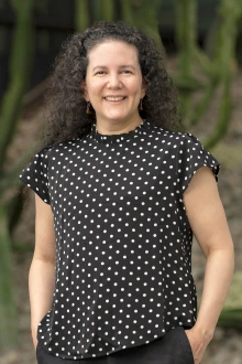 Portrait of woman with dark, curly hair. She is wearing a black top with white polka dots.