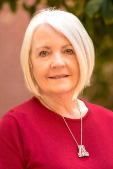 Portrait of Dr. Cindy Rishel wearing a red blouse and University of Arizona "A" necklace.