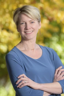 Portrait of Felicia Goodrum, a white woman with short blonde hair standing with arms crossed and smiling.
