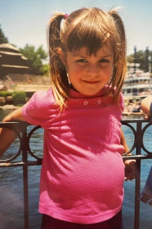 candid photo of a young girl leaning against a railing with a body of water in the background