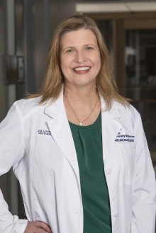 Female doctor wearing a white coat and green blouse stands in a hallway on the College of Medicine – Tucson campus.