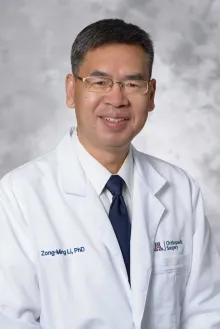 Professor Zong-Ming Li smiling and wearing a blue tie and white lab coat. 