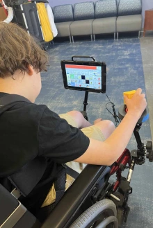 Boy in wheelchair uses a switch to control his communication device.