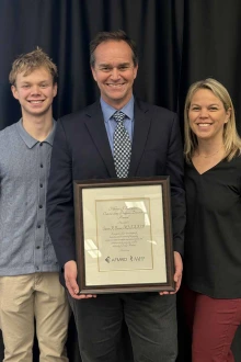 Steven Brown, MD, stand between his son Andrew and his wife Molly holding a framed certificate.