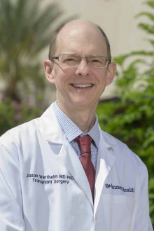 Portrait of Jason Wertheim, MD, PhD, in a white doctor’s coat standing outside.