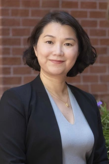 Portrait of Silvia Xu standing outside in front of some flowers and a brick building.