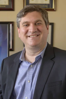 Portrait of Michael Grandner in front of a wall lined with framed photos and certificates.
