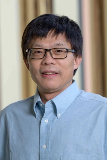 Portrait of professor Wei Wang wearing a blue button-up shirt and smiling.