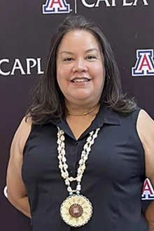 Portrait of Christina C. Bell Andrews, JD, MPH, MBA, MA, with a medal around her neck in front of a background with the University of Arizona College of Architecture, Planning and Landscape Architecture logo.