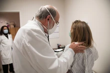 doctor listening to patient's lungs, nurse standing in doorway