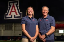 two people stand in an athletic space with a University of Arizona logo in the background