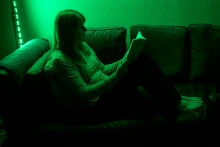 green lighting shines on a person sitting on a couch reading a book