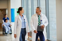 two doctors talk while walking down a hospital hallway