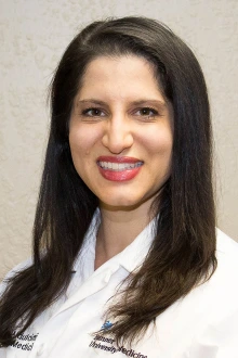 Portrait of Dr. Sommer Aldulaimi. A woman with dark brown hair wearing a white doctor's coat.