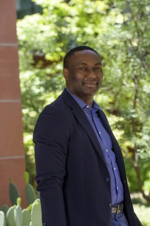 Black man wearing a suit, standing outside and smiling.