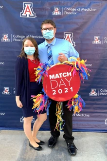 A man and woman (Tyler and Claire Pascavis) pose together while holding a sign that says "Match Day 2021."