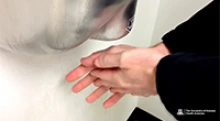 A person using a warm-air electric hand dryer after washing their hands. (Photo: University of Arizona Health Sciences)