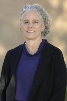 Portrait of a smiling light-skinned woman with curly gray hair standing outside. 