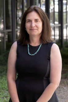 White woman with shoulder-length brown hair wearing a black dress standing outside.