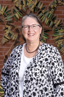 Portrait of a middle-aged white woman with salt and pepper hair wearing glasses and smiling. 