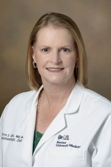 Blonde woman wearing a white medical coat sits for a portrait.