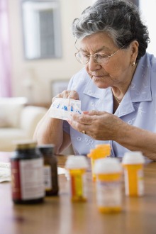 An older adult woman sits at a table to take her medications.