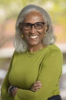 Portrait of Juanita Merchant, a Black woman with shoulder-lenght gray hair, wearing a green blouse and smiling. 