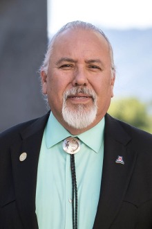 Portrait of Dr. Carlos Gonzales standing outsice in a dark suit coat and bolo tie.