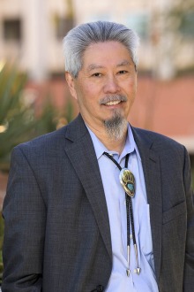 Portrait of a man standing outside wearing a suit coat and a bolo tie. 