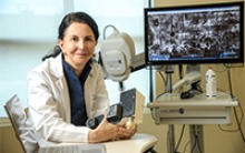 Dr. Clara Curiel Lewandrowski in front of a screen showing the images produced by a confocal microscope. She holds the smaller, portable version she is developing for wider use by doctors. (Photo: Kris Hanning/ University of Arizona Health Sciences)