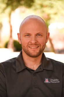 Bald man wearing a University of Arizona Disability Resources Center t-shirt standing outside