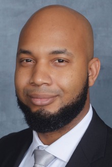 Portrait of a Black man with a beard wearing a black suit, white dress shirt and silver tie