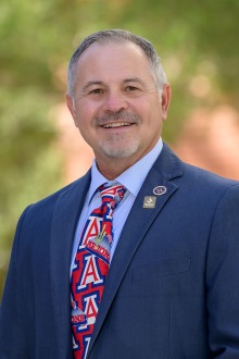 A portrait of UArizona College of Nursing professor Jim Reed wearing a suit and tie and smiling in an outdoor setting.