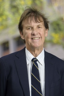 Smiling older man wearing a black suit and tie standing outside.